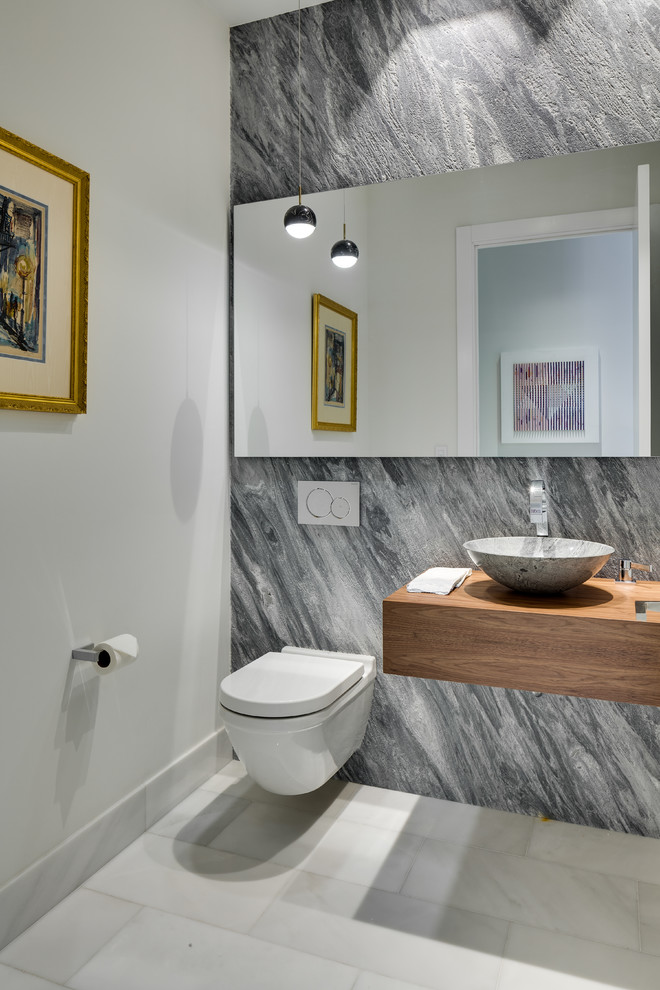Aménagement d'un WC suspendu contemporain de taille moyenne avec un carrelage gris, des dalles de pierre, un mur gris, un sol en marbre, une vasque, un plan de toilette en bois, un sol blanc et un plan de toilette marron.