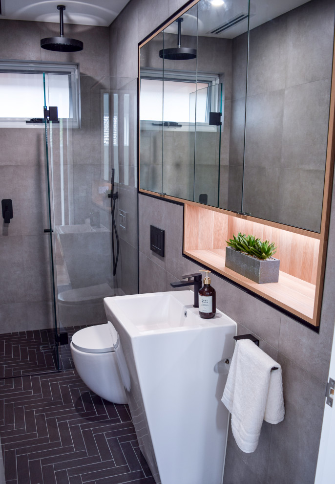 Modern inredning av ett litet vit vitt badrum, med en vägghängd toalettstol, grå kakel, porslinskakel, klinkergolv i porslin, ett piedestal handfat, svart golv, vita skåp, grå väggar och träbänkskiva