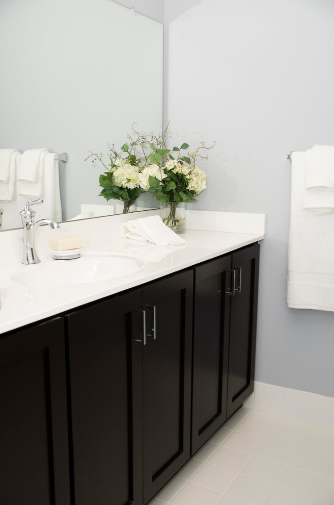 Esempio di un bagno di servizio classico di medie dimensioni con ante in stile shaker, ante nere, pareti grigie, pavimento con piastrelle in ceramica, lavabo integrato, top in superficie solida, pavimento bianco e top bianco