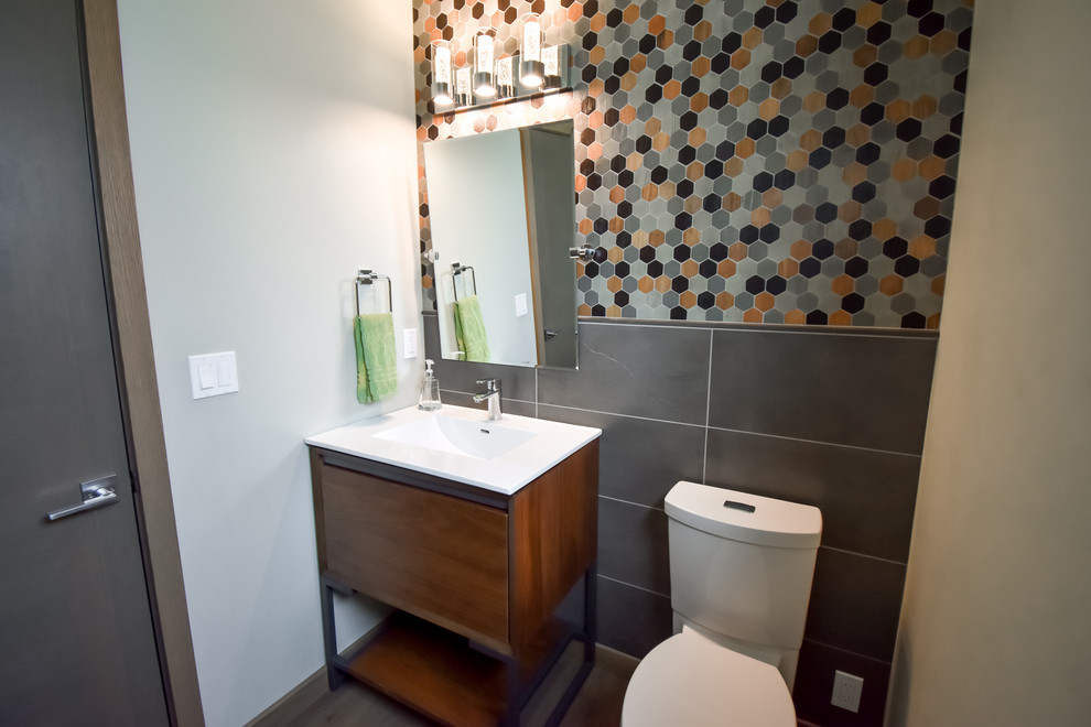 Exempel på ett litet modernt toalett, med släta luckor, skåp i mörkt trä, en toalettstol med separat cisternkåpa, blå väggar, ett piedestal handfat, svart kakel och mellanmörkt trägolv