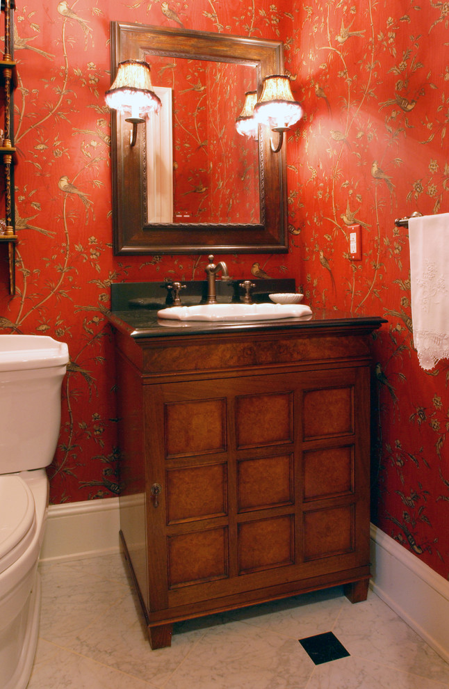 Foto på ett litet vintage toalett, med ett nedsänkt handfat, möbel-liknande, skåp i mellenmörkt trä, granitbänkskiva, röda väggar och marmorgolv
