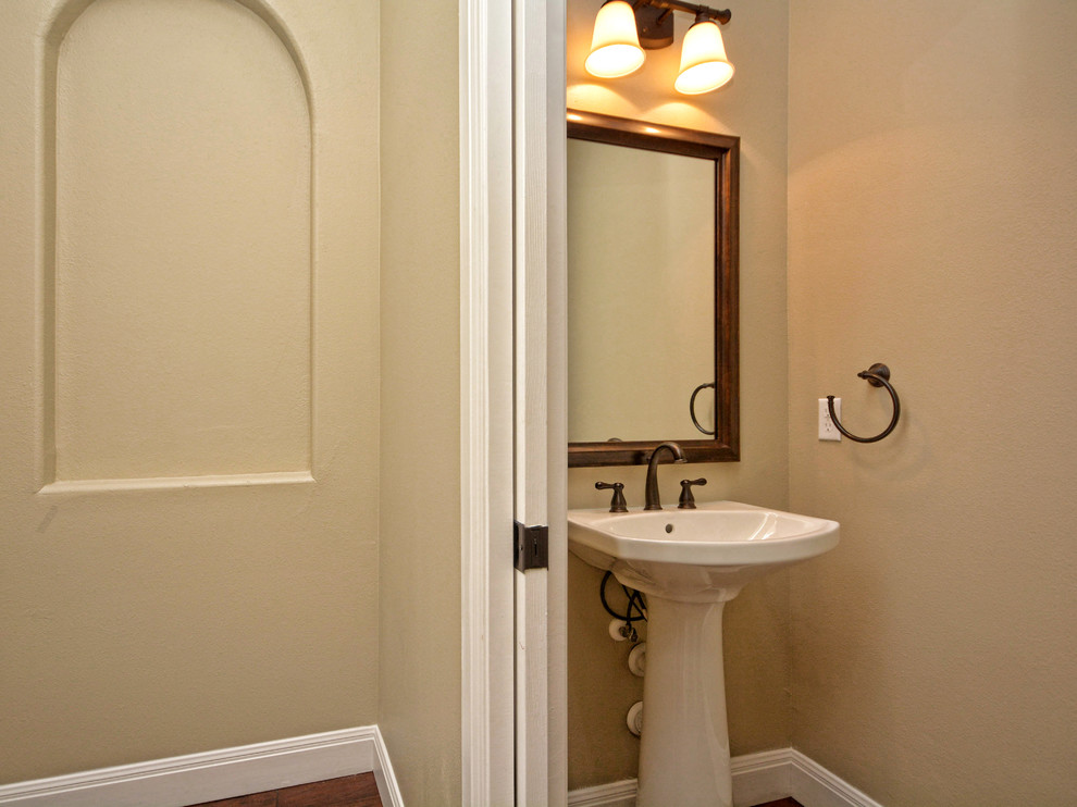 Modelo de aseo clásico de tamaño medio con paredes beige, suelo de madera en tonos medios y lavabo con pedestal