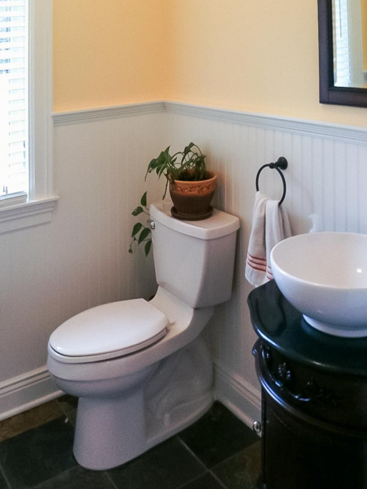 Inspiration för svart toaletter, med möbel-liknande, skåp i mörkt trä, en toalettstol med separat cisternkåpa, gula väggar, skiffergolv, ett fristående handfat, granitbänkskiva och flerfärgat golv
