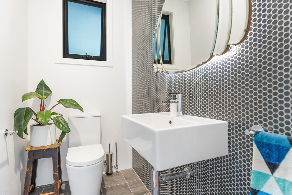 Modern inredning av ett vit vitt toalett, med vita skåp, en toalettstol med separat cisternkåpa, svart och vit kakel, porslinskakel, svarta väggar, klinkergolv i porslin, ett avlångt handfat, bänkskiva i akrylsten och grått golv