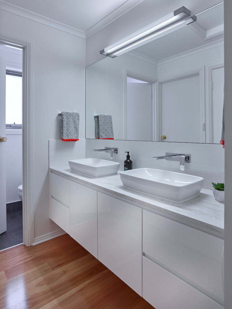 Example of a mid-sized trendy white tile medium tone wood floor powder room design in Other with white cabinets, white walls and a vessel sink