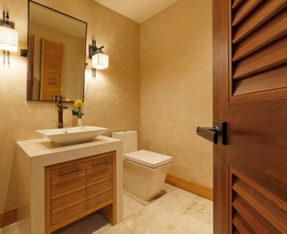 Cette image montre un WC et toilettes design en bois clair de taille moyenne avec un placard à porte plane, WC à poser, un mur beige, un sol en travertin, une vasque, un plan de toilette en calcaire et un sol beige.