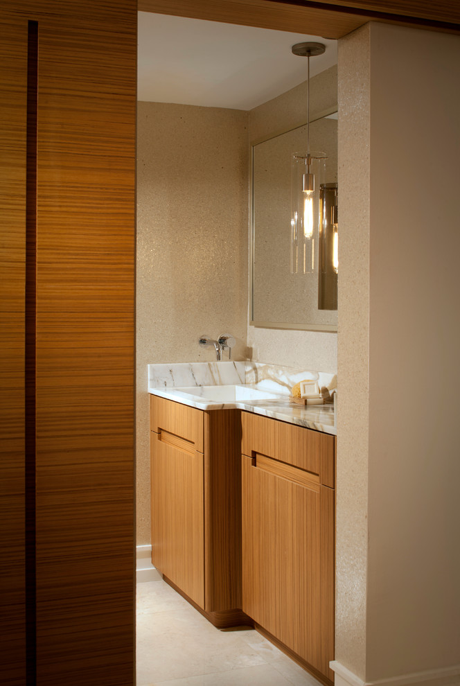 Cette photo montre un WC et toilettes bord de mer en bois brun avec un lavabo intégré, un placard à porte plane, un plan de toilette en marbre, WC séparés et un carrelage beige.