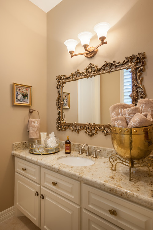 Bathroom cabinets with granite countertops in a traditional vanity design with ornate framed mirror and warm lighting