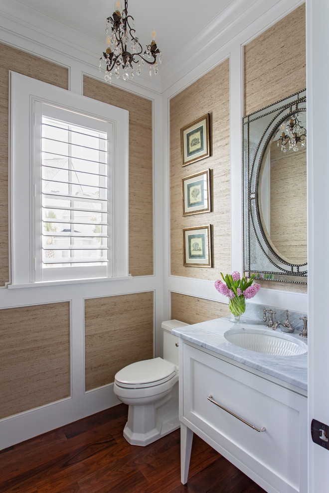 This is an example of a medium sized beach style cloakroom in Charleston with beaded cabinets, white cabinets, a one-piece toilet, beige walls, medium hardwood flooring, marble worktops, brown floors and grey worktops.