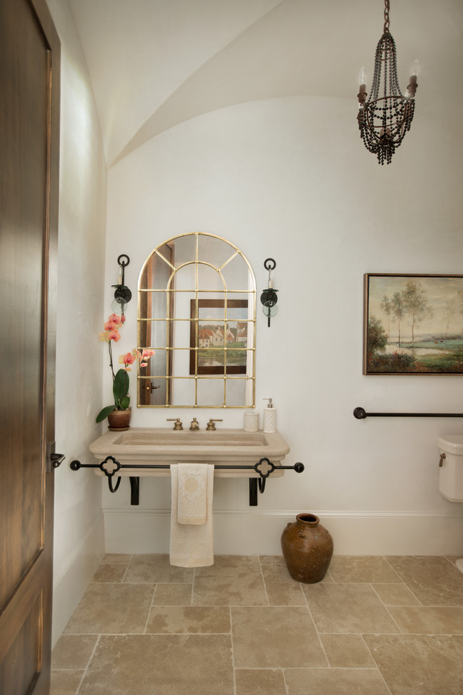 Пример оригинального дизайна: большой туалет в средиземноморском стиле с раздельным унитазом, бежевой плиткой, каменной плиткой, бежевыми стенами, полом из известняка, подвесной раковиной и столешницей из известняка