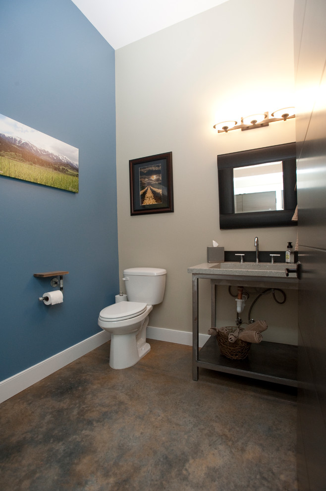 他の地域にある高級な広いインダストリアルスタイルのおしゃれなトイレ・洗面所 (中間色木目調キャビネット、一体型トイレ	、グレーのタイル、グレーの壁、コンクリートの床、一体型シンク、再生グラスカウンター) の写真