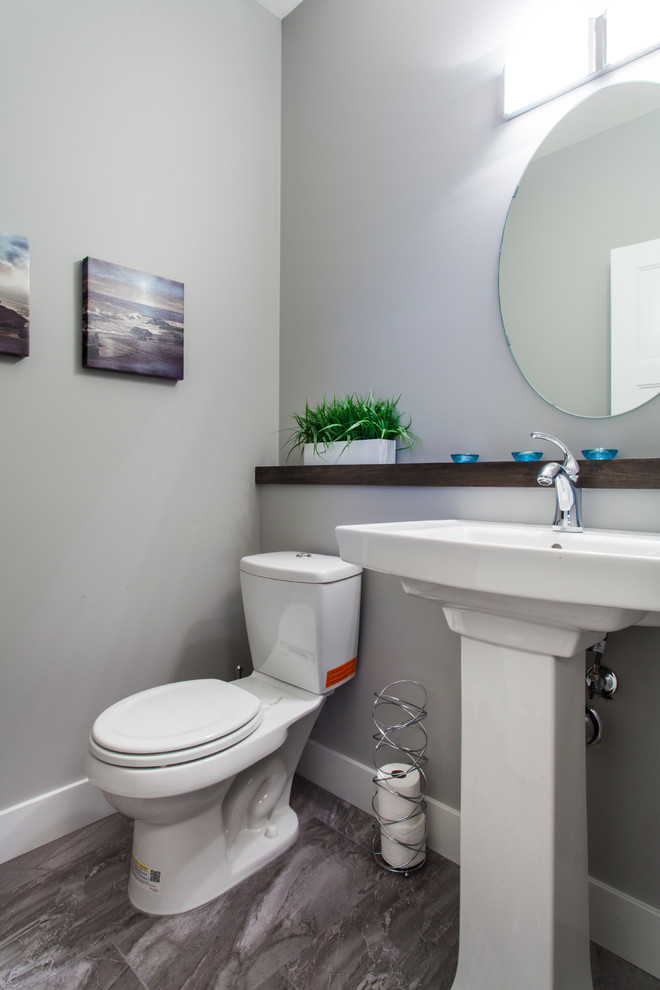 Modelo de aseo contemporáneo, pequeño, con lavabo con pedestal, sanitario de dos piezas, baldosas y/o azulejos grises, paredes grises y suelo de baldosas de cerámica