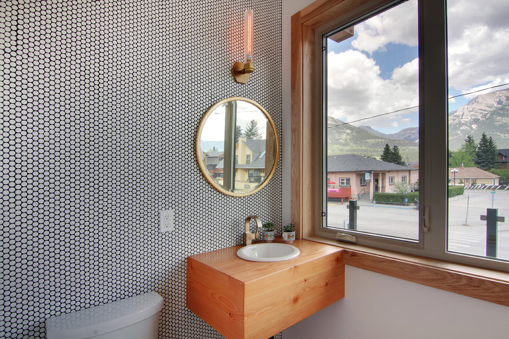 Пример оригинального дизайна: туалет среднего размера в современном стиле с черно-белой плиткой, серыми стенами, накладной раковиной, фасадами цвета дерева среднего тона, столешницей из дерева и коричневой столешницей