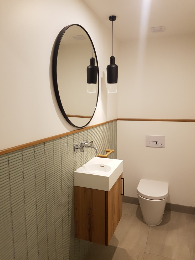 На фото: туалет среднего размера в современном стиле с фасадами цвета дерева среднего тона, унитазом-моноблоком, зеленой плиткой, стеклянной плиткой, подвесной раковиной, столешницей из талькохлорита и подвесной тумбой с