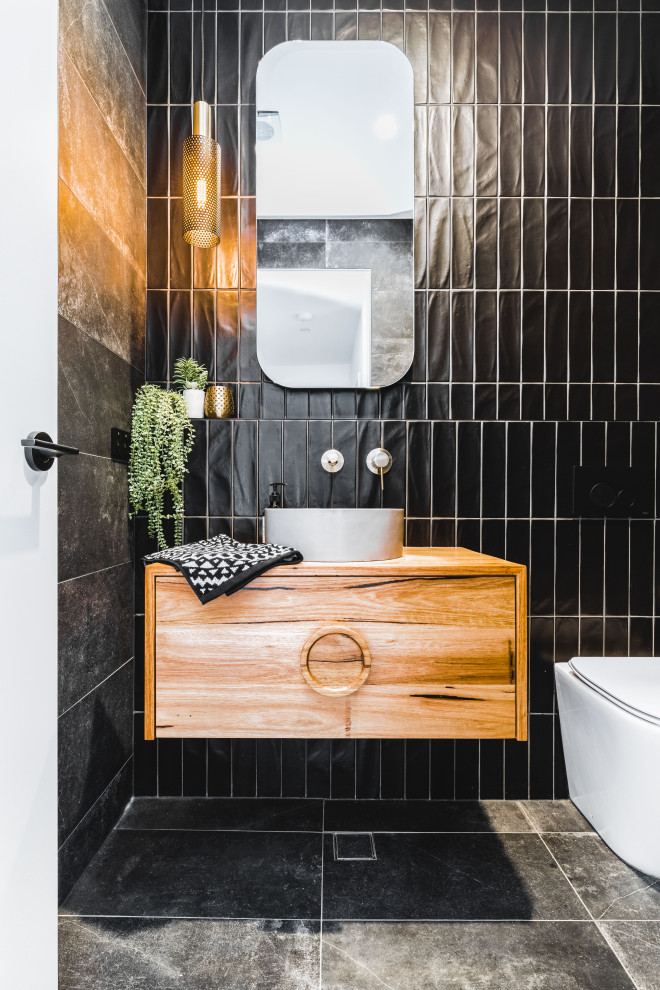 Kleine Moderne Gästetoilette mit schwarzen Fliesen, flächenbündigen Schrankfronten, hellbraunen Holzschränken, Toilette mit Aufsatzspülkasten, Aufsatzwaschbecken, Waschtisch aus Holz, grauem Boden, brauner Waschtischplatte und schwebendem Waschtisch in Sydney