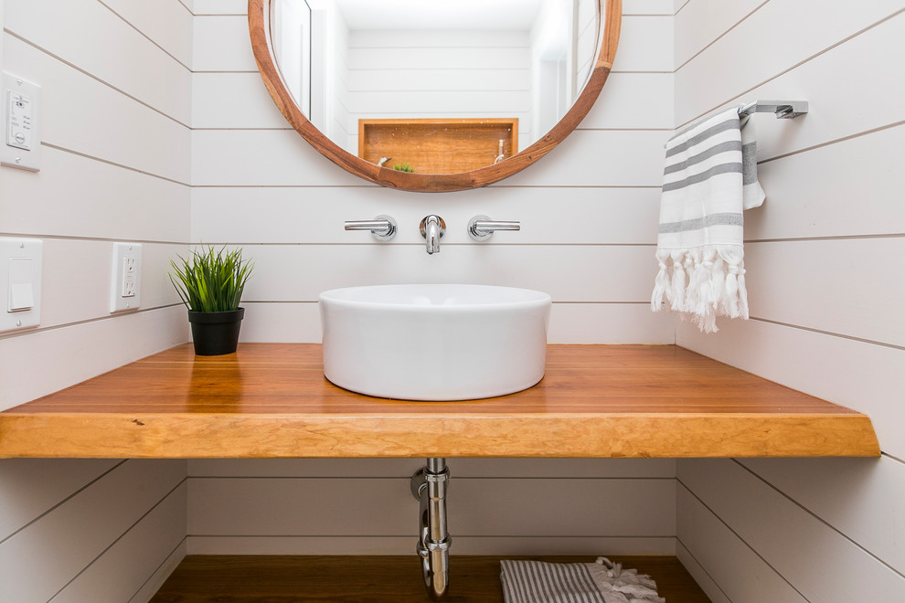 Photo of a small farmhouse cloakroom in Ottawa with a wall mounted toilet, white walls, light hardwood flooring, a vessel sink and wooden worktops.