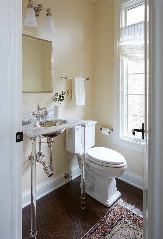 Cette photo montre un petit WC et toilettes chic avec un placard sans porte, WC à poser, un mur beige, parquet foncé, un lavabo encastré, un sol marron, un plan de toilette en marbre et un plan de toilette blanc.