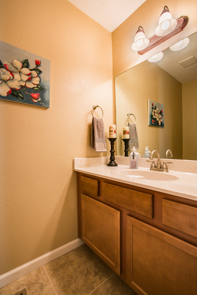 Große Klassische Gästetoilette mit Schrankfronten im Shaker-Stil, hellbraunen Holzschränken, Wandtoilette mit Spülkasten, beigen Fliesen, Keramikfliesen, beiger Wandfarbe, Keramikboden, integriertem Waschbecken und Mineralwerkstoff-Waschtisch in Albuquerque