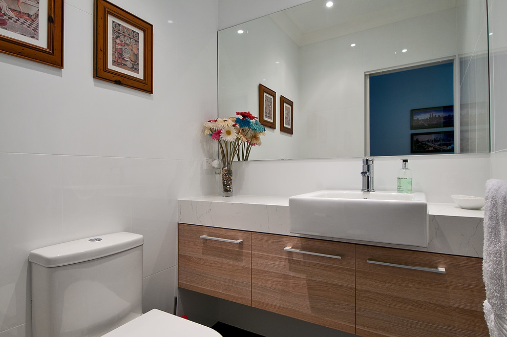 Idee per un piccolo bagno di servizio moderno con lavabo da incasso, ante lisce, ante in legno chiaro, top in quarzo composito, WC monopezzo, piastrelle bianche, piastrelle in ceramica e pareti bianche