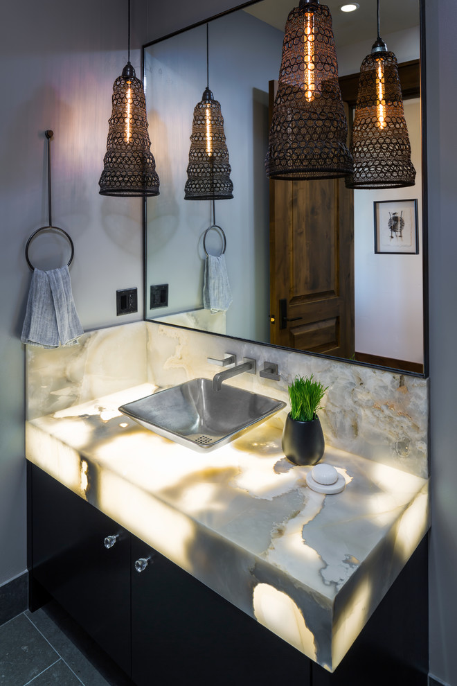 Powder room - mid-sized rustic porcelain tile and gray floor powder room idea in Other with flat-panel cabinets, black cabinets, a one-piece toilet, gray walls, a vessel sink and onyx countertops