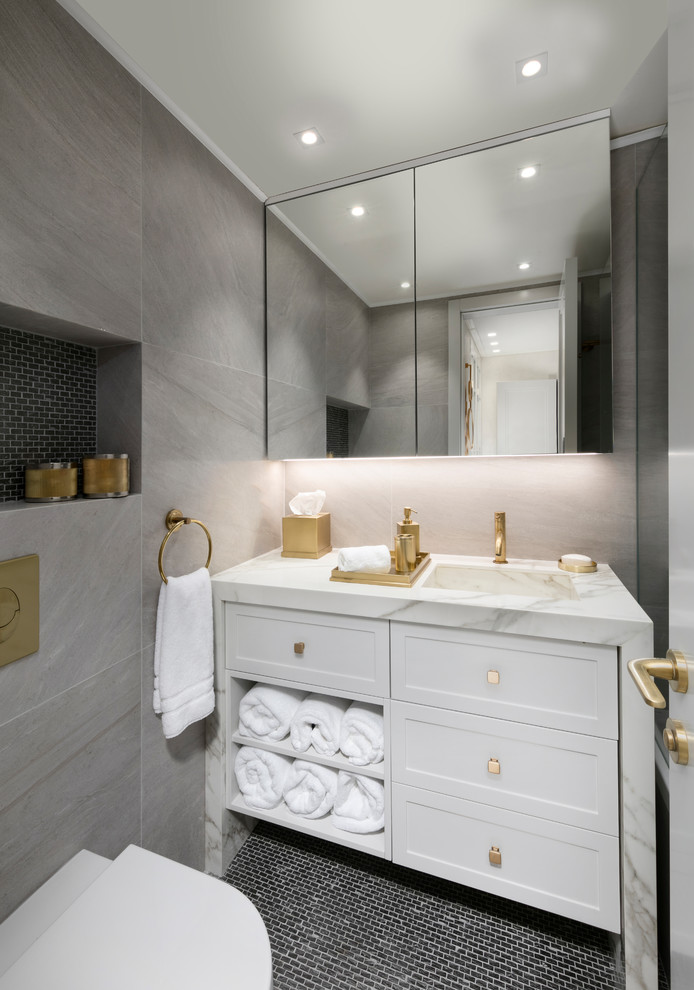 Immagine di un bagno di servizio minimal con ante in stile shaker, ante bianche, WC monopezzo, piastrelle grigie, pavimento con piastrelle a mosaico, lavabo integrato, pavimento nero e top bianco