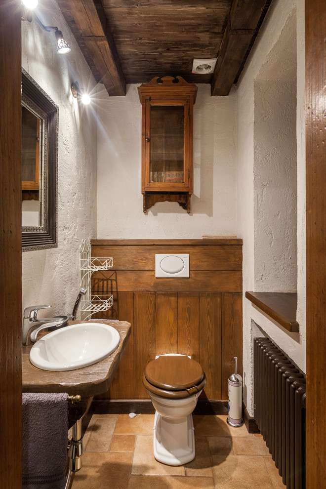 Foto på ett litet rustikt brun toalett, med ett nedsänkt handfat, vita väggar, en toalettstol med separat cisternkåpa och brunt golv