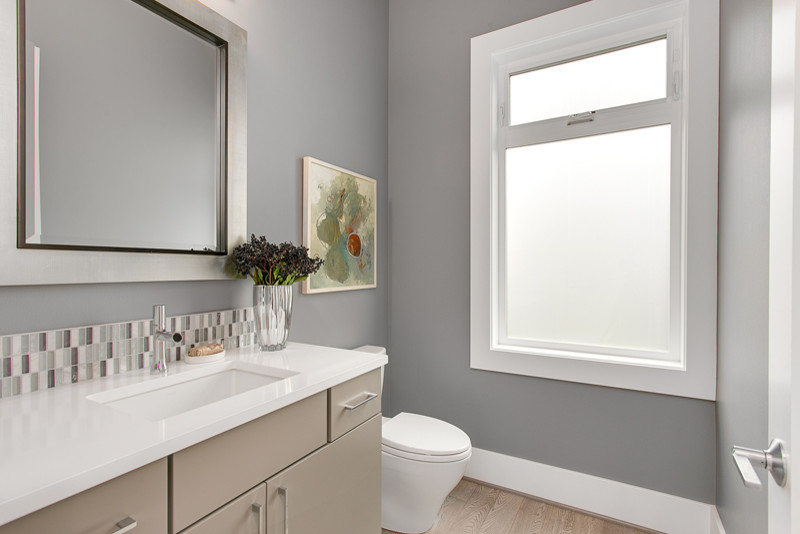 Medium sized contemporary cloakroom in Seattle with flat-panel cabinets, medium wood cabinets, a two-piece toilet, multi-coloured tiles, glass tiles, grey walls, light hardwood flooring, a submerged sink, engineered stone worktops and white worktops.