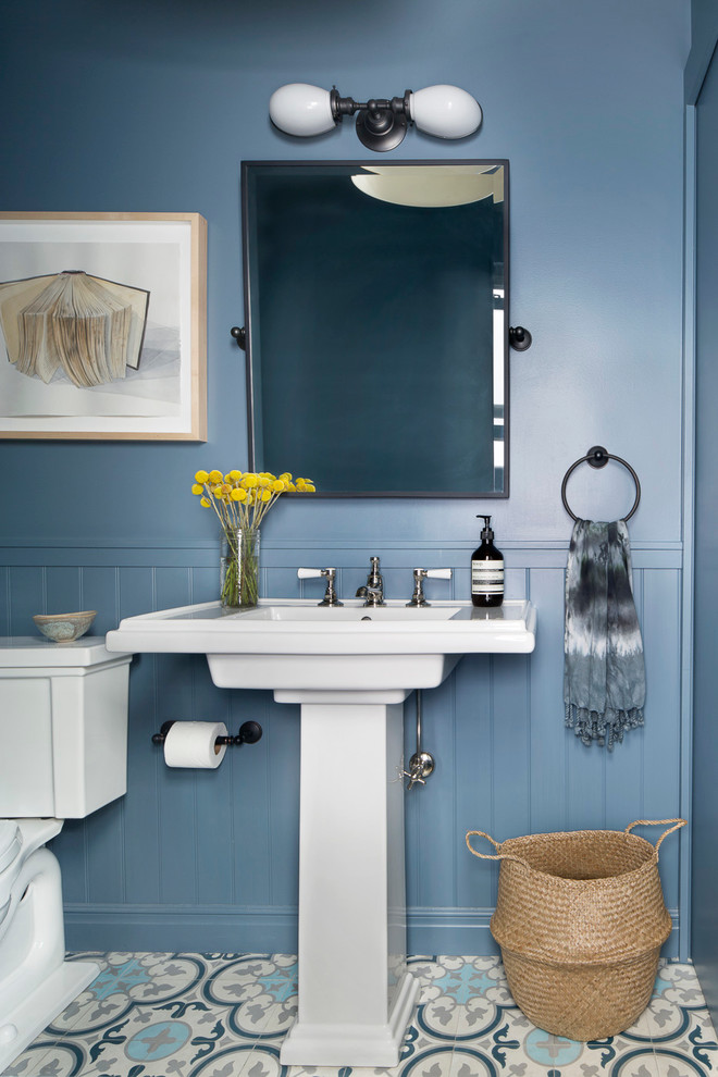 Klassisk inredning av ett litet toalett, med en toalettstol med separat cisternkåpa, blå väggar, ett piedestal handfat, flerfärgat golv och cementgolv