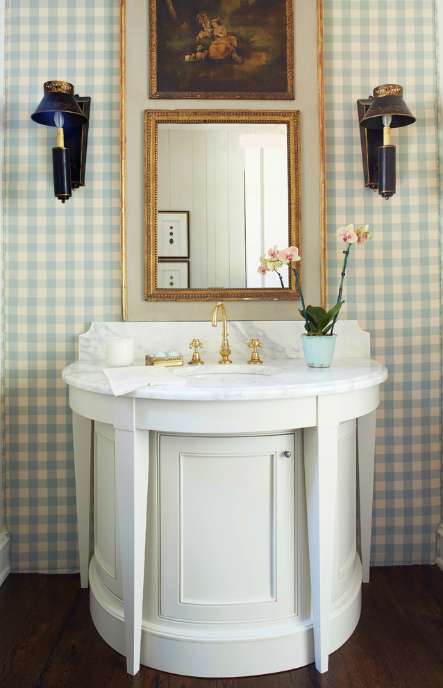 Inredning av ett klassiskt litet vit vitt toalett, med luckor med profilerade fronter, vita skåp, blå väggar, mörkt trägolv, marmorbänkskiva, brunt golv och ett undermonterad handfat