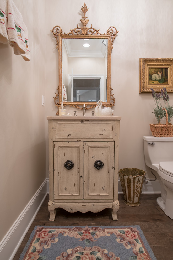 Foto di un bagno di servizio classico di medie dimensioni con consolle stile comò, ante con finitura invecchiata, WC monopezzo, pareti beige, parquet scuro e lavabo sottopiano
