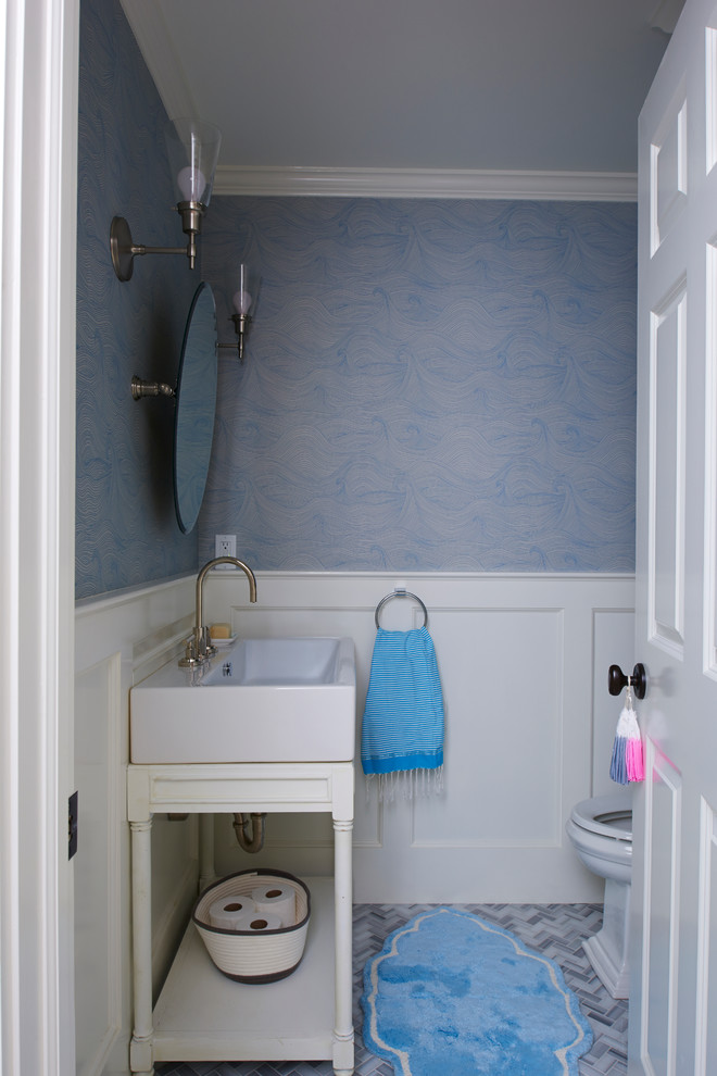 Inredning av ett maritimt litet toalett, med en toalettstol med separat cisternkåpa, grå kakel, klinkergolv i keramik, blå väggar och ett fristående handfat