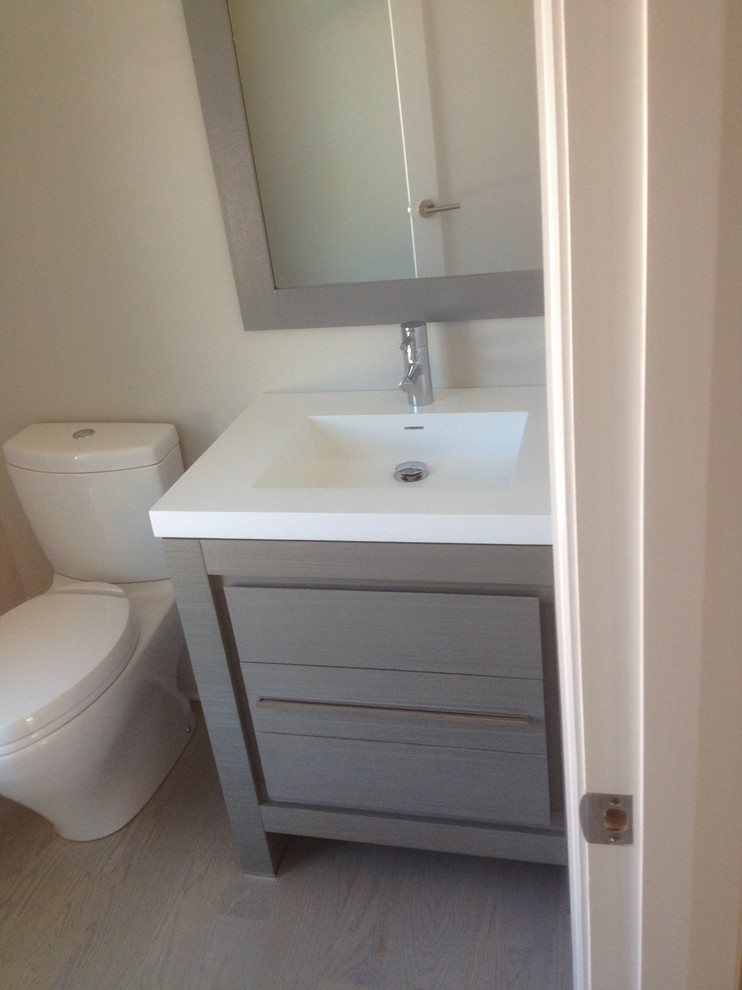 Idéer för små funkis toaletter, med släta luckor, grå skåp, vita väggar, ett integrerad handfat, bänkskiva i akrylsten och en toalettstol med separat cisternkåpa