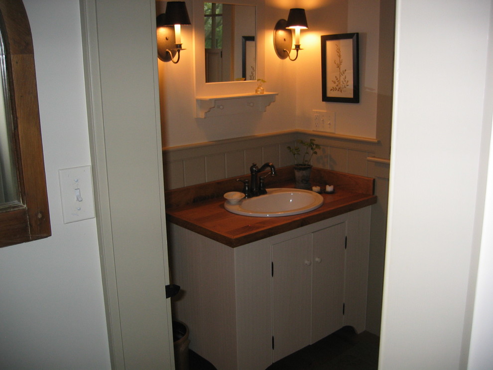 Kleine Country Gästetoilette mit flächenbündigen Schrankfronten, weißen Schränken, weißer Wandfarbe, Einbauwaschbecken, Waschtisch aus Holz und brauner Waschtischplatte in Boston