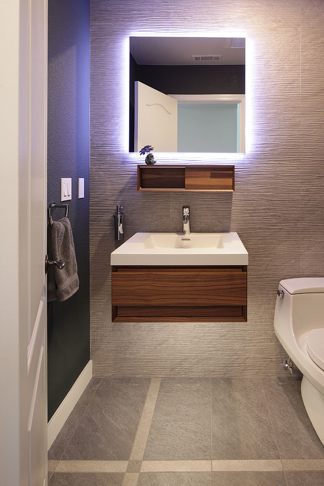 Example of a small trendy gray tile and porcelain tile porcelain tile and gray floor powder room design in San Francisco with flat-panel cabinets, dark wood cabinets, a one-piece toilet, green walls, an integrated sink, solid surface countertops and white countertops
