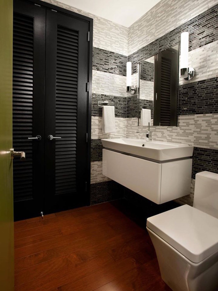 Пример оригинального дизайна: туалет среднего размера в современном стиле с белыми фасадами, унитазом-моноблоком, черной плиткой, серой плиткой, белой плиткой, плиткой мозаикой, паркетным полом среднего тона, разноцветными стенами и подвесной раковиной