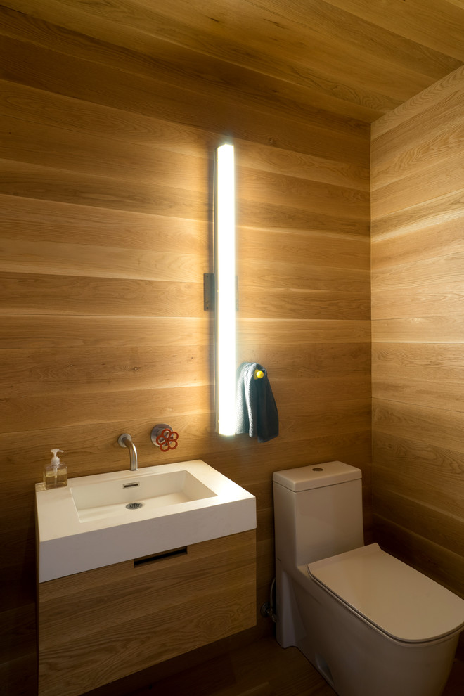 Imagen de aseo moderno pequeño con armarios con paneles lisos, puertas de armario de madera clara, sanitario de una pieza, paredes marrones, suelo de madera clara, lavabo suspendido y suelo marrón