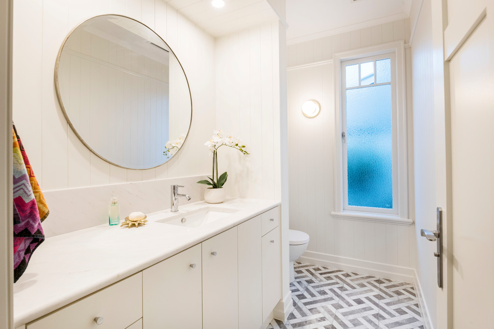 Cette photo montre un WC et toilettes chic de taille moyenne avec WC à poser, un mur blanc, un sol en marbre, un lavabo encastré, un plan de toilette en marbre, un sol gris et un plan de toilette blanc.
