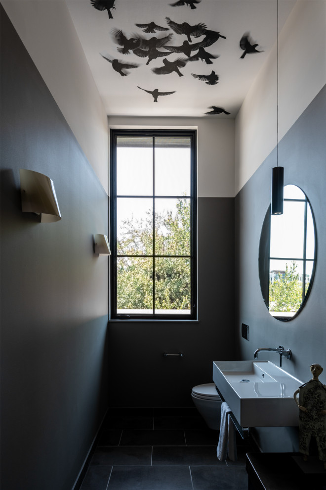 Exemple d'un WC et toilettes tendance de taille moyenne avec WC à poser, un mur gris, un sol en carrelage de céramique, un lavabo suspendu et un sol gris.