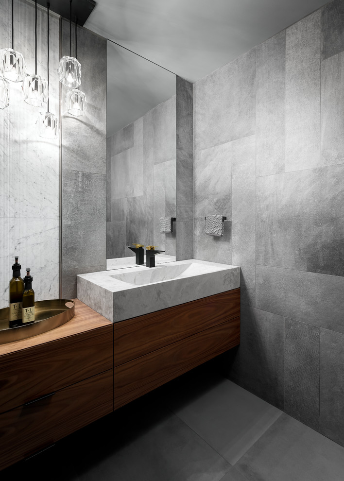 Idée de décoration pour un WC et toilettes design en bois brun avec un placard à porte plane, un carrelage gris, un mur gris, une vasque, un plan de toilette en bois et un sol gris.