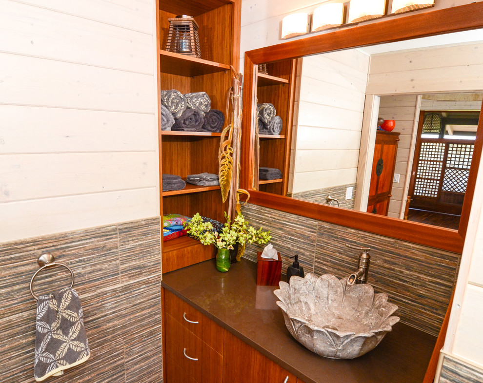 ハワイにある中くらいなトロピカルスタイルのおしゃれなトイレ・洗面所 (ベッセル式洗面器、フラットパネル扉のキャビネット、クオーツストーンの洗面台、グレーのタイル、セラミックタイル、白い壁、中間色木目調キャビネット) の写真