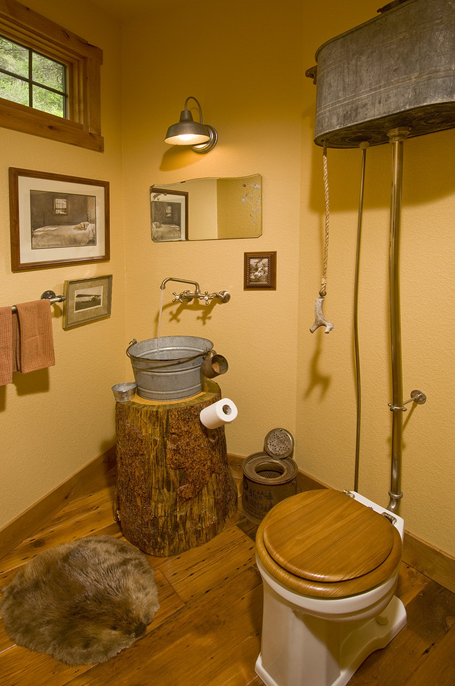 Kleine Rustikale Gästetoilette mit hellbraunen Holzschränken, Toilette mit Aufsatzspülkasten, gelber Wandfarbe, dunklem Holzboden und Aufsatzwaschbecken in Denver
