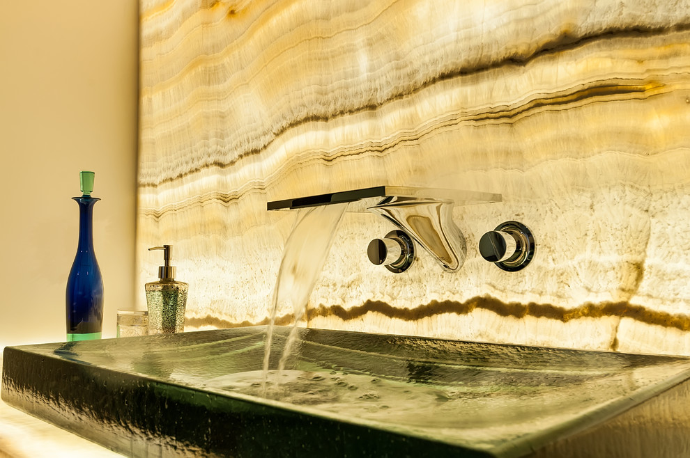 ロサンゼルスにあるラグジュアリーな広いコンテンポラリースタイルのおしゃれなトイレ・洗面所 (フラットパネル扉のキャビネット、茶色いキャビネット、一体型トイレ	、白いタイル、石スラブタイル、大理石の床、ベッセル式洗面器、オニキスの洗面台、ベージュの床) の写真