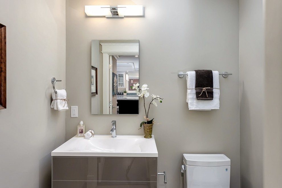 Klassisk inredning av ett litet toalett, med släta luckor, grå skåp, en toalettstol med separat cisternkåpa, grå väggar och ett integrerad handfat