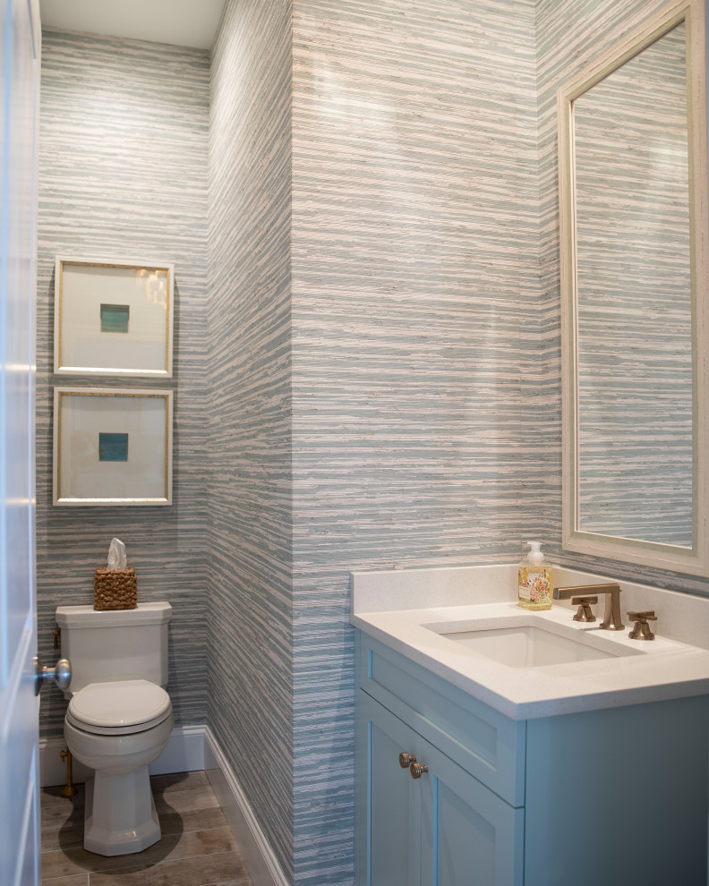На фото: туалет в стиле неоклассика (современная классика) с фасадами в стиле шейкер, синими фасадами, серыми стенами, темным паркетным полом, врезной раковиной, коричневым полом, белой столешницей, встроенной тумбой и обоями на стенах с