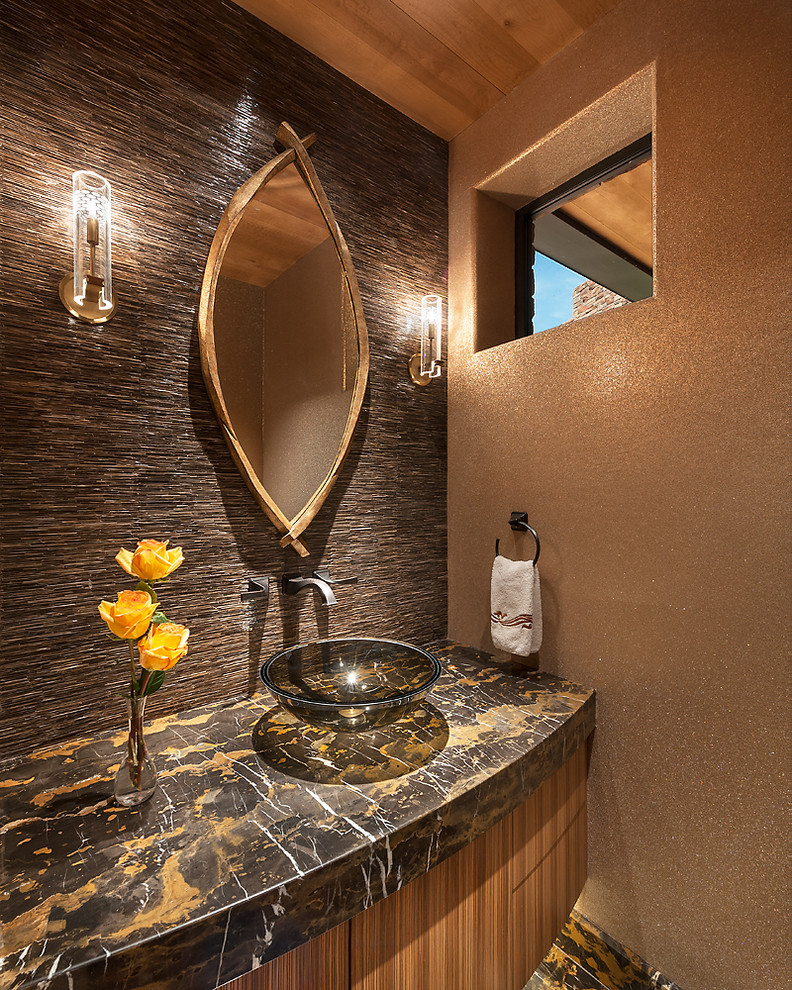 Amerikansk inredning av ett stort toalett, med skåp i mellenmörkt trä, ett fristående handfat, möbel-liknande, brun kakel, stenkakel, marmorgolv och marmorbänkskiva