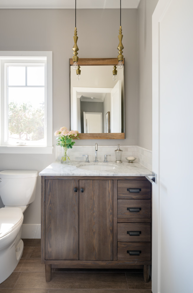 Cette image montre un WC et toilettes traditionnel en bois brun de taille moyenne avec un placard à porte plane, WC séparés, un mur gris, un sol en carrelage de porcelaine, un lavabo encastré, un plan de toilette en marbre et un plan de toilette blanc.