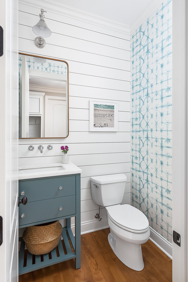 シカゴにある高級な広いトランジショナルスタイルのおしゃれなトイレ・洗面所 (フラットパネル扉のキャビネット、白い壁、茶色い床、白い洗面カウンター、青いキャビネット、分離型トイレ、無垢フローリング、コンソール型シンク) の写真