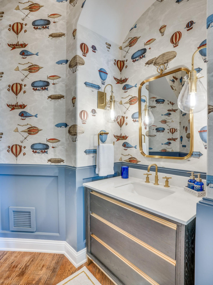Photo of a classic cloakroom in Dallas with flat-panel cabinets, grey cabinets, multi-coloured walls, medium hardwood flooring, a submerged sink, brown floors, white worktops, a freestanding vanity unit, wainscoting and wallpapered walls.