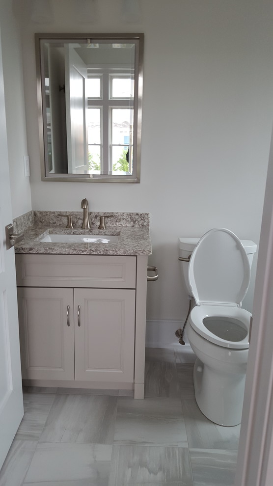 Exemple d'un petit WC et toilettes chic avec un lavabo encastré, un placard avec porte à panneau encastré, des portes de placard beiges, un plan de toilette en quartz modifié, WC à poser, un mur gris et un sol en marbre.