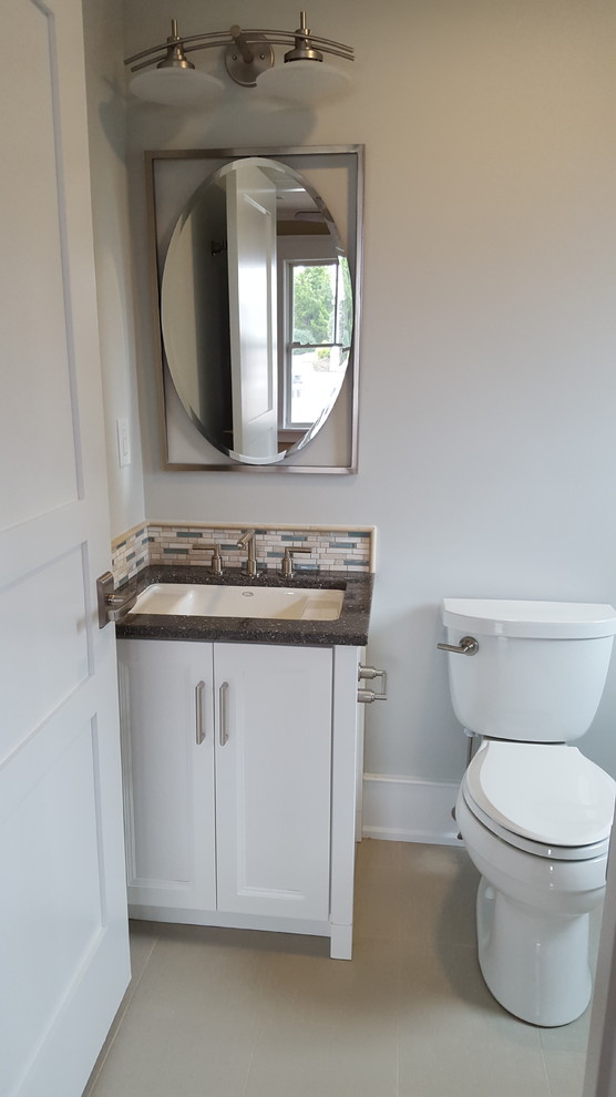 Klassisk inredning av ett mellanstort toalett, med ett undermonterad handfat, luckor med infälld panel, vita skåp, bänkskiva i kvarts, en toalettstol med hel cisternkåpa, flerfärgad kakel, glaskakel, grå väggar och klinkergolv i keramik